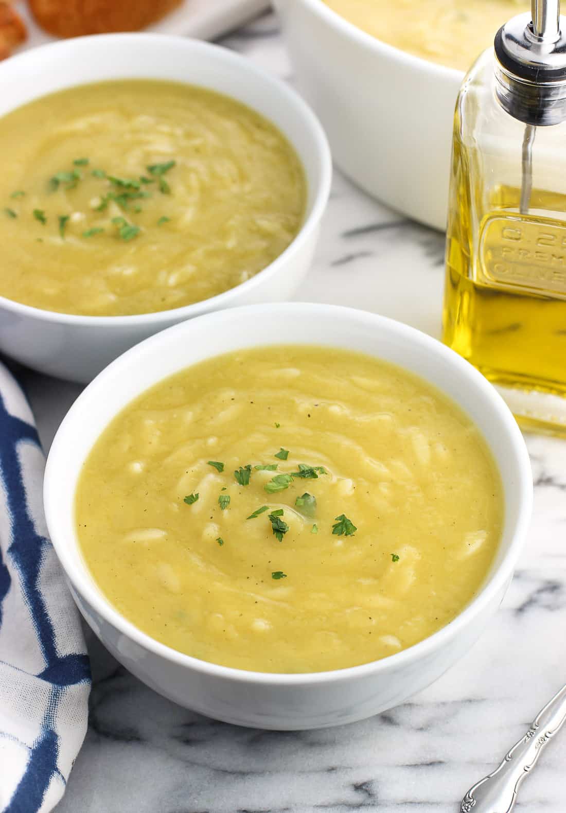 Two bowls of soup garnished with fresh herbs in front of a glass olive oil dispenser.