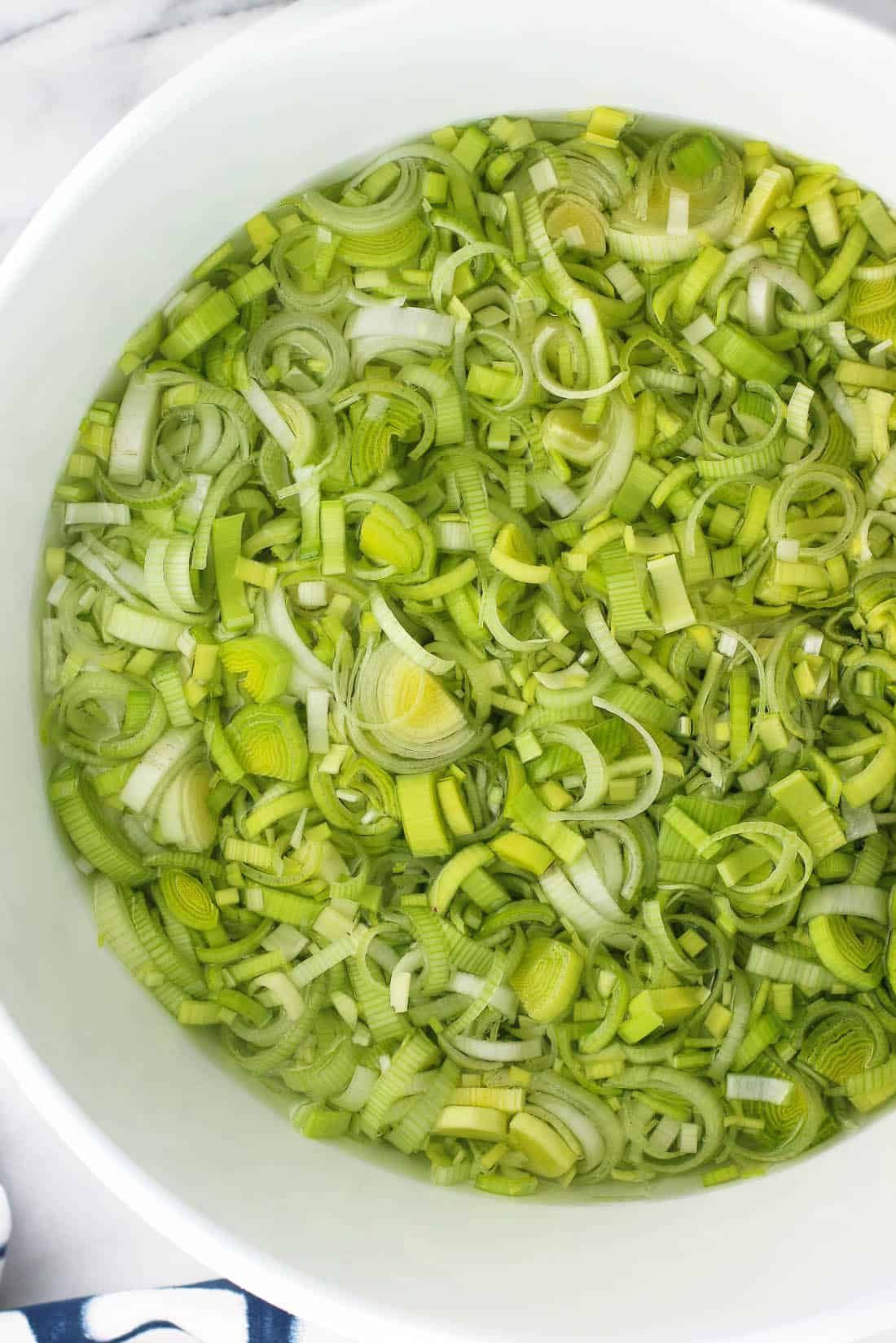 Thinly-sliced leeks in a large plastic bowl of water.