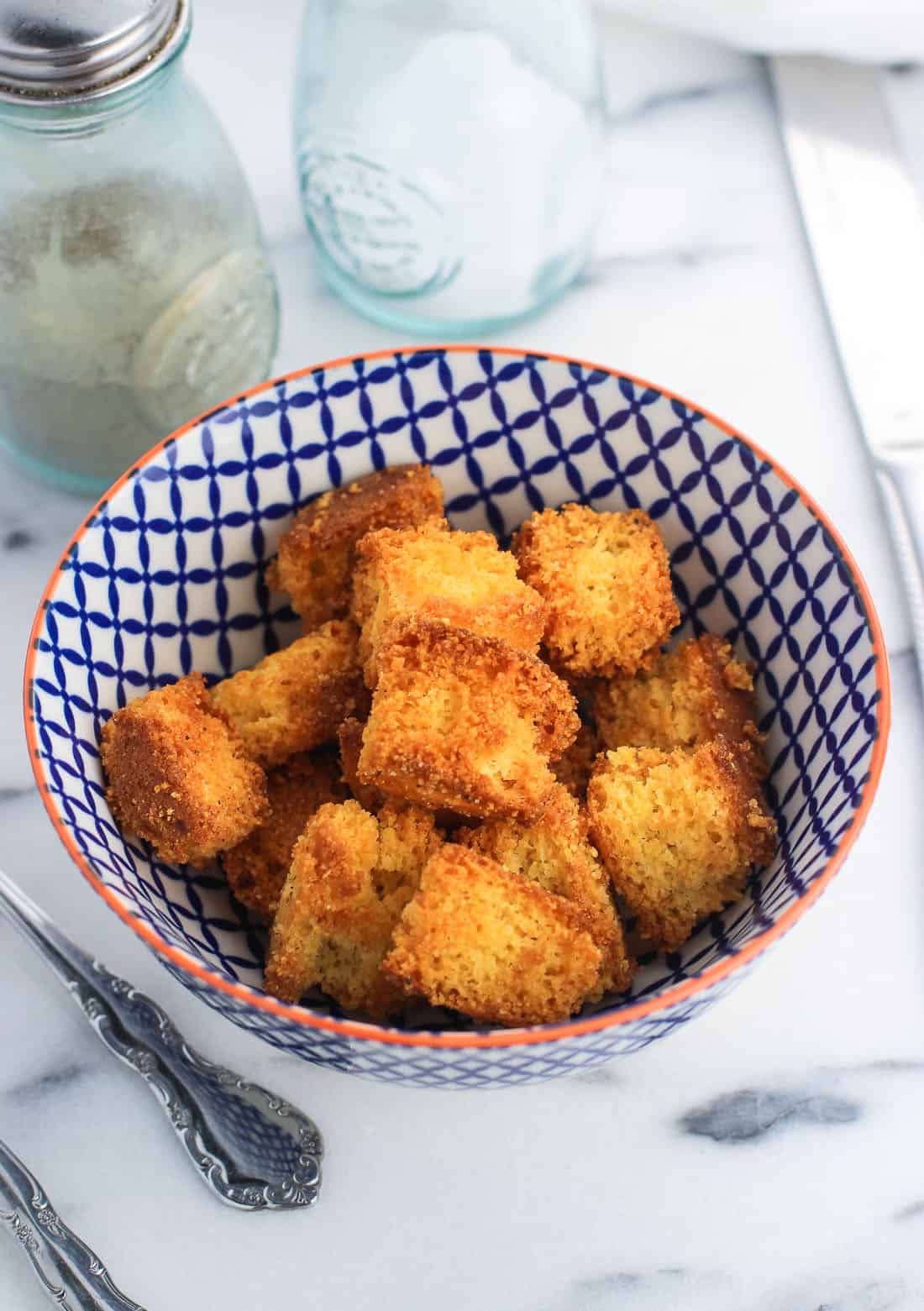 Croutons in a small ceramic bowl next to utensils and salt and pepper shakers