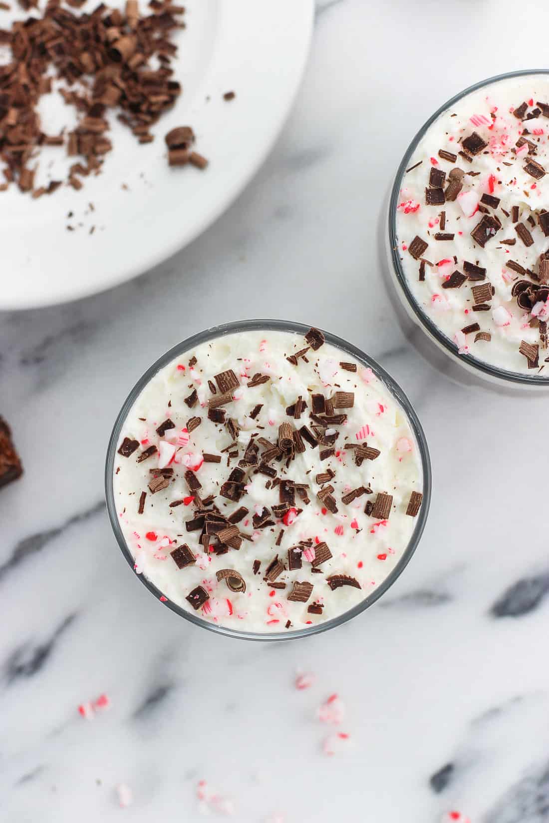 An overhead picture of two small glass jars of trifle with a plate of chocolate shavings in the background