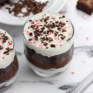 A close-up picture of a serving of trifle in a small glass, topped with chocolate shavings and crushed candy cane pieces