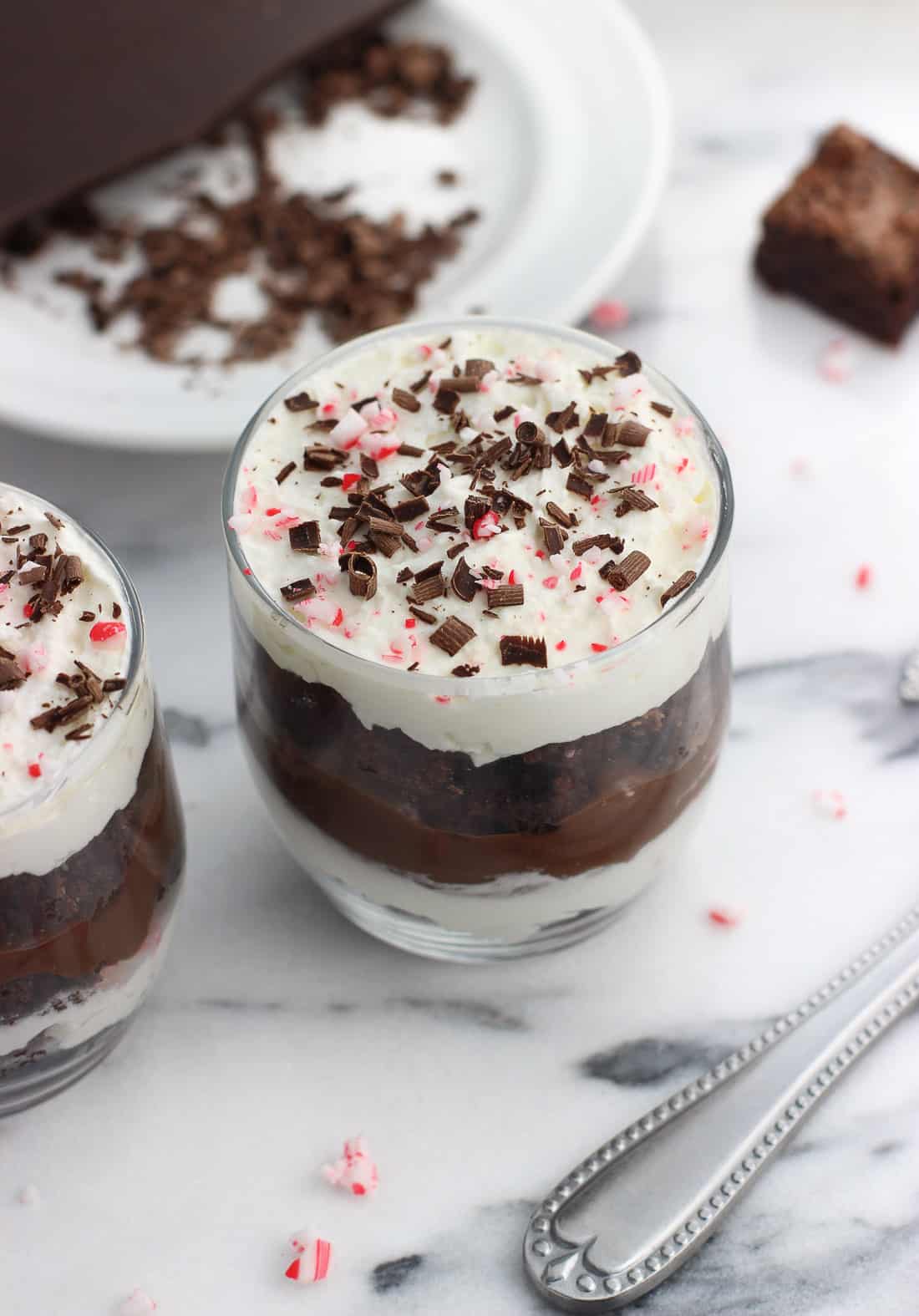 A close-up picture of a serving of trifle in a small glass, topped with chocolate shavings and crushed candy cane pieces