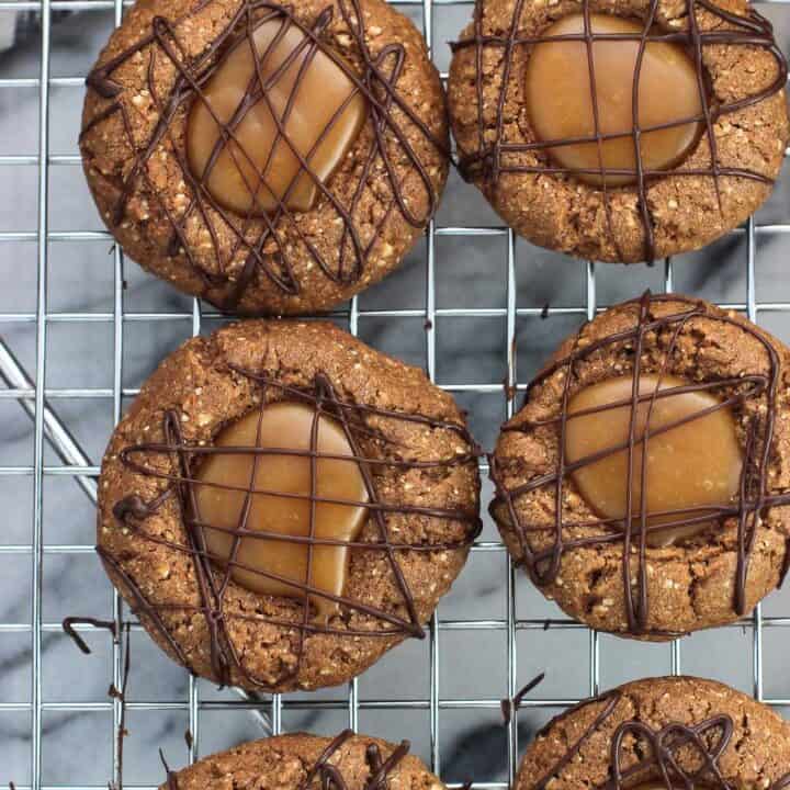 An overhead picture of thumbprint cookies drizzled with chocolate on a metal wire cooling rack