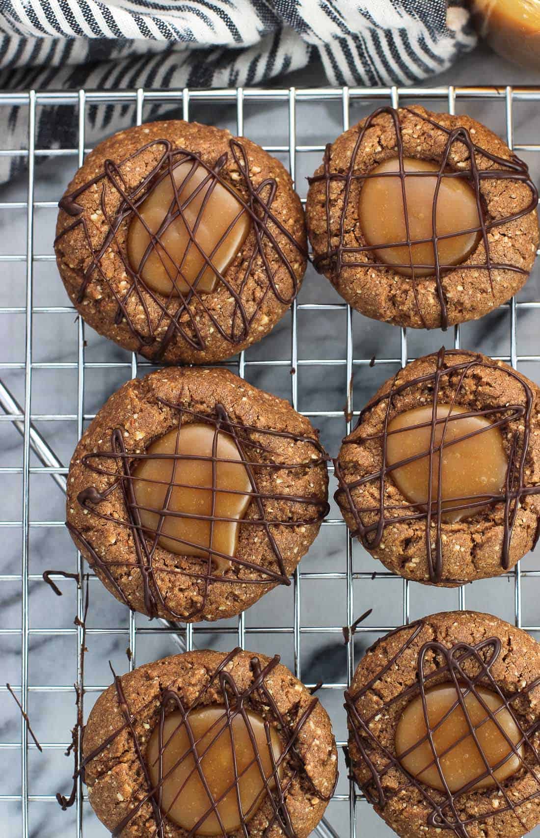 An overhead picture of thumbprint cookies drizzled with chocolate on a metal wire cooling rack
