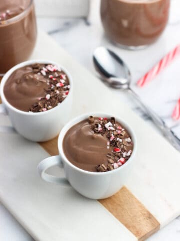 Two ceramic demitasse cups filled with pudding and garnished with a swirl of chocolate shavings and crushed candy canes