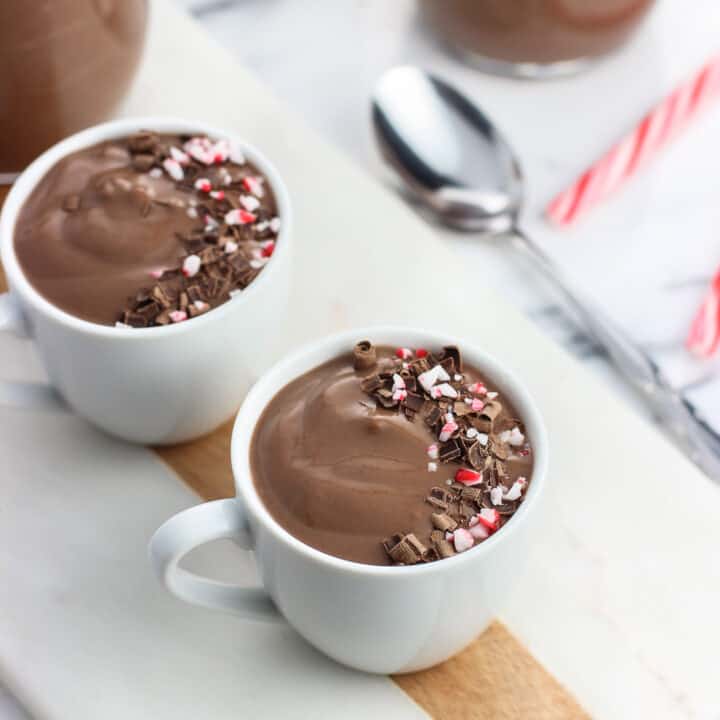 Two ceramic demitasse cups filled with pudding and garnished with a swirl of chocolate shavings and crushed candy canes