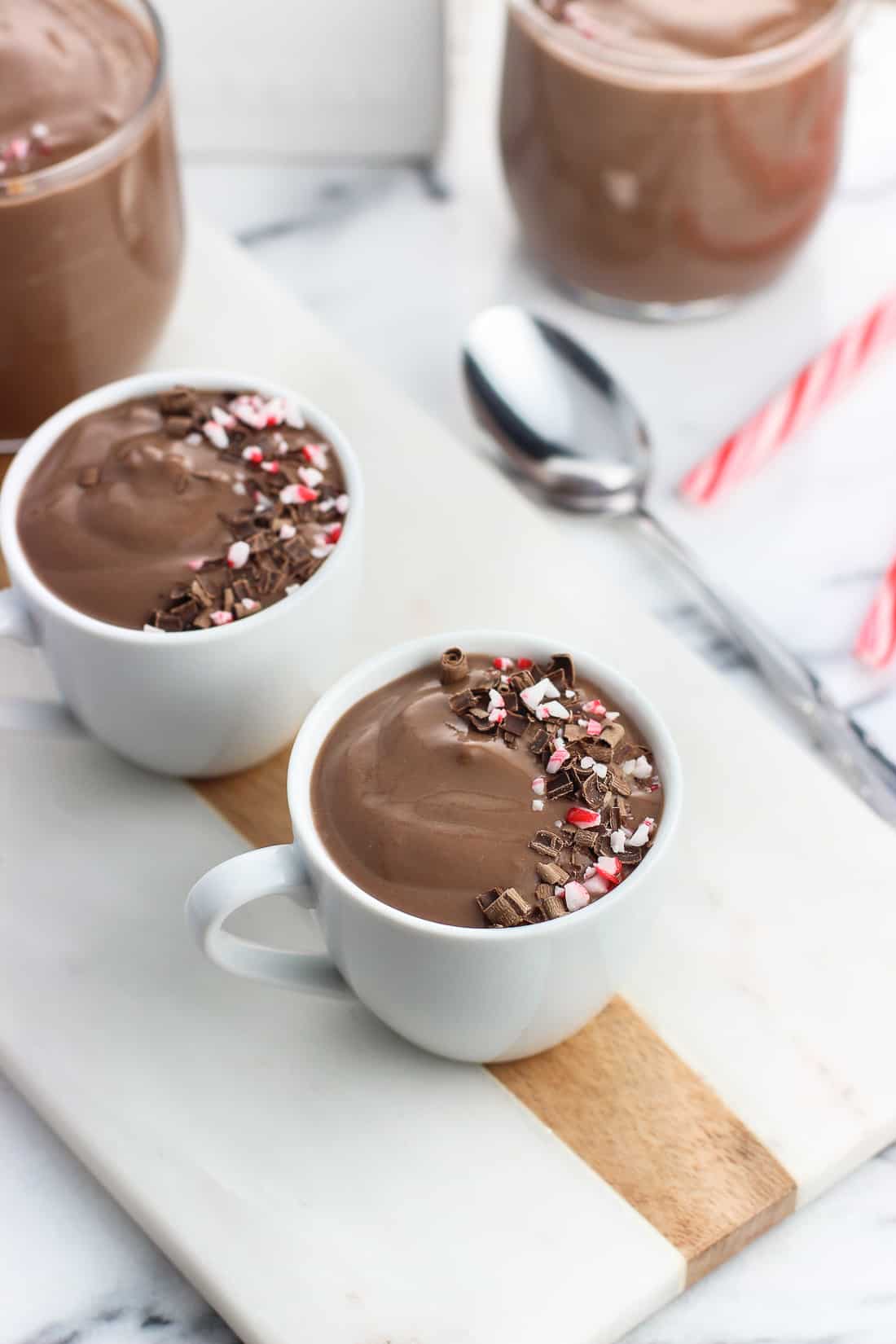 Two ceramic demitasse cups filled with pudding and garnished with a swirl of chocolate shavings and crushed candy canes