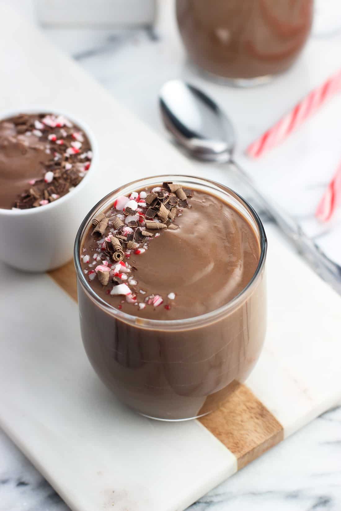 A glass filled with pudding and garnished with a swirl of chocolate shavings and crushed candy cane pieces