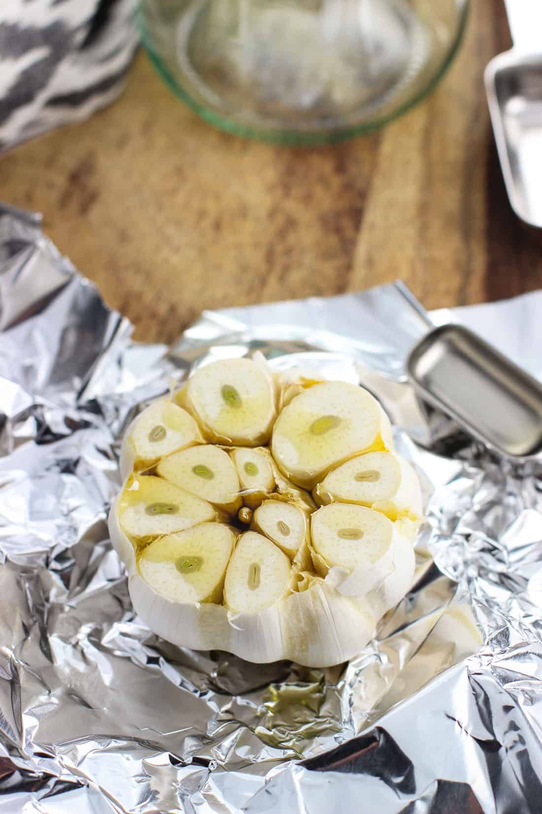 A head of raw garlic with the top portion sliced off drizzled with olive oil on a piece of aluminum foil