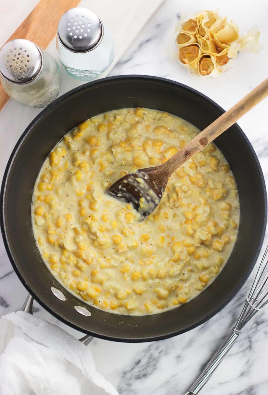 The creamed corn in the saucepan after adding back the blended portion, with a wooden spoon sticking out of the pan