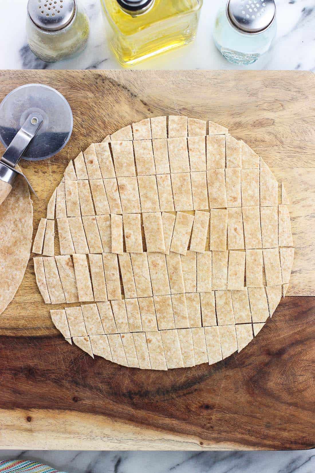 A tortilla sliced into small rectangular pieces on a wooden cutting board.