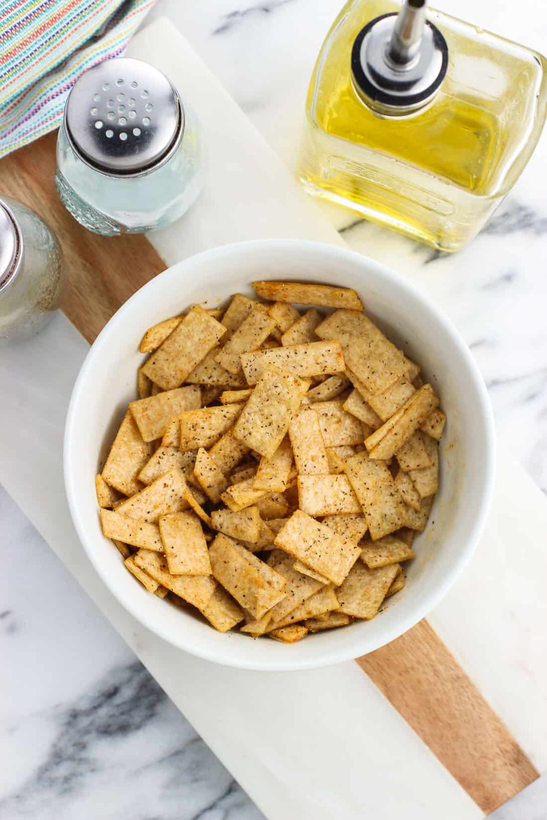 Tortilla strips in a bowl tossed with oil before being baked.