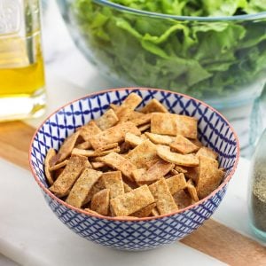 A bowl of tortilla strips in front of various salad ingredients.