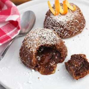 Two mini lava cakes on a plate with a bite removed from the front cake to show the filling.