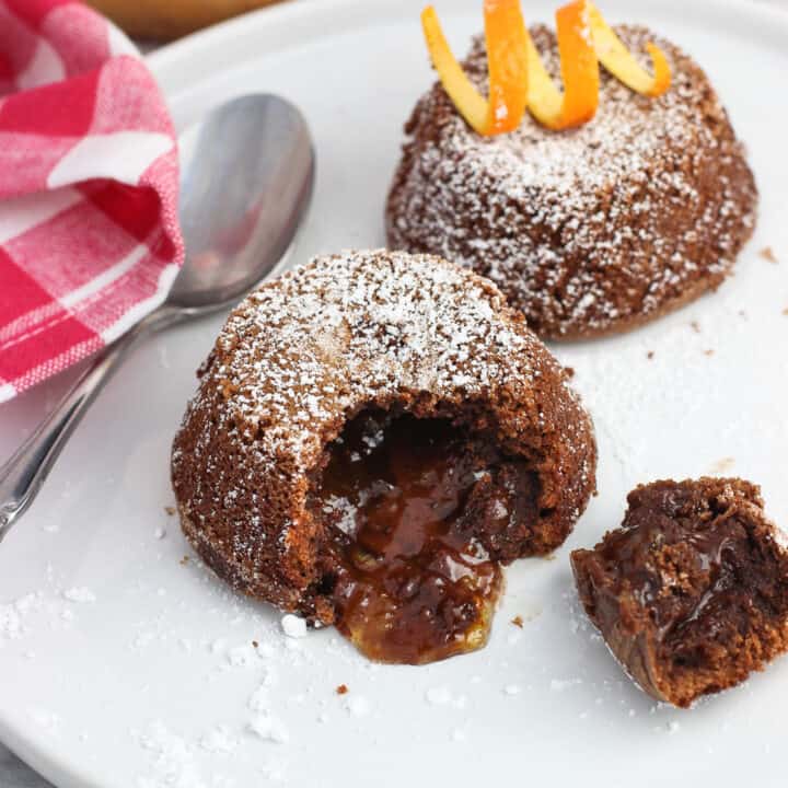 Two mini lava cakes on a plate with a bite removed from the front cake to show the filling.