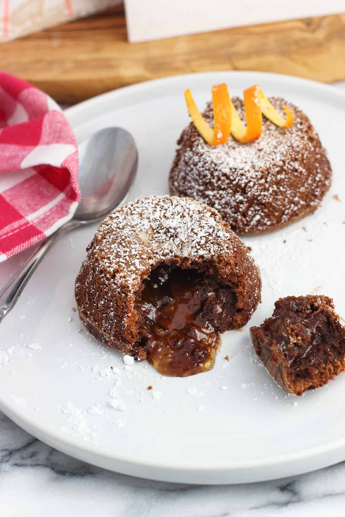 Two mini lava cakes on a plate with a bite removed from the front cake to show the filling.