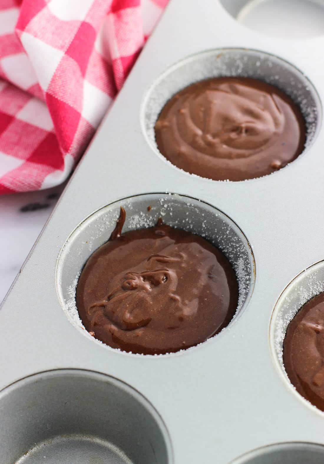 Lava cake batter poured into buttered and sugared metal muffin tin wells