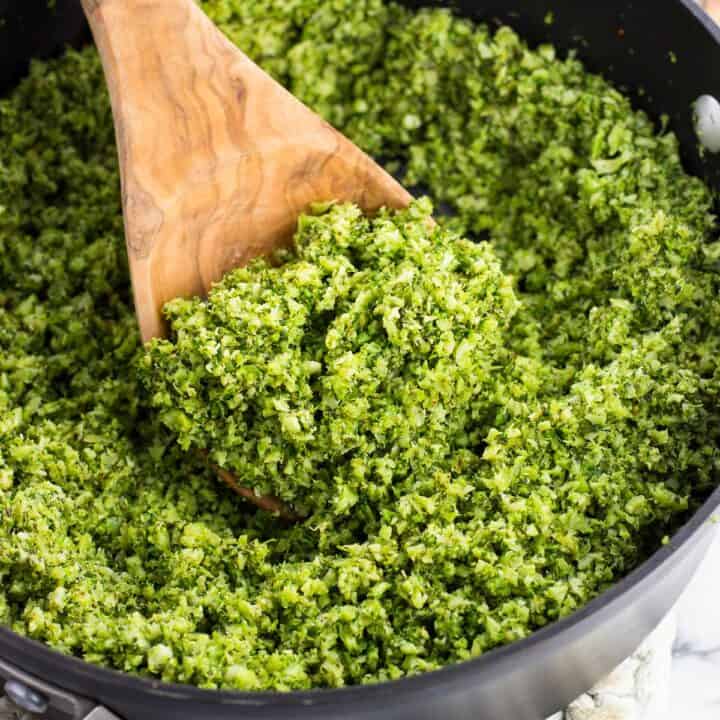 Pesto broccoli rice in a pan with a wooden spoon scooping it.
