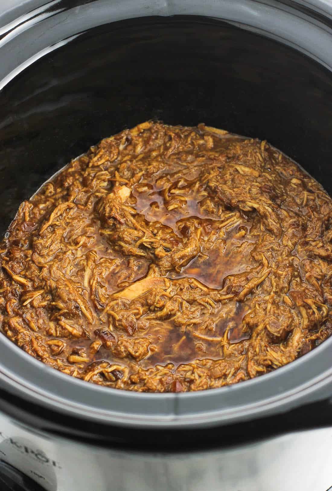 A slow cooker filled with shredded chicken and sauce.
