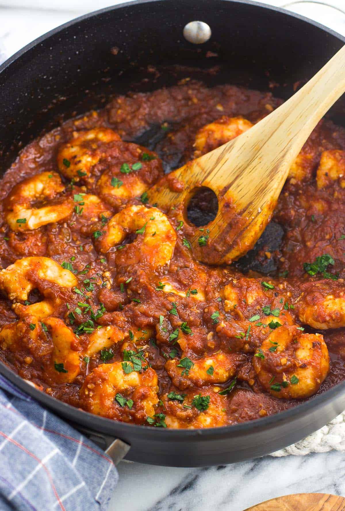 Cooked jumbo shrimp in fra diavolo sauce in a skillet garnished with fresh parsley.