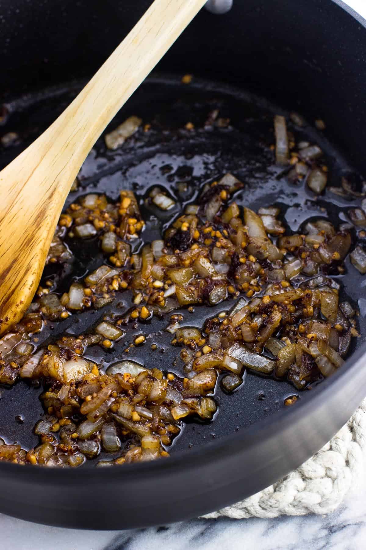 Diced onion and minced garlic sauteed in bacon grease in a pan with a wooden spoon.