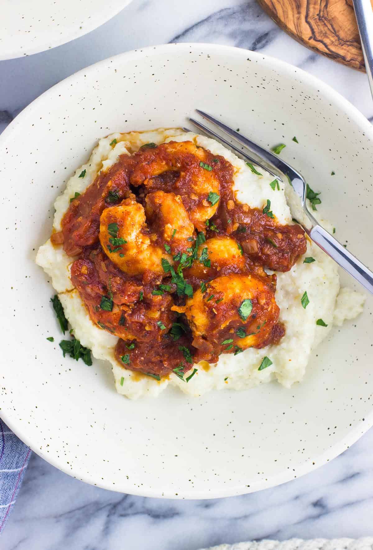 An overhead shot of shrimp fra diavolo served over grits in a shallow bowl with a fork