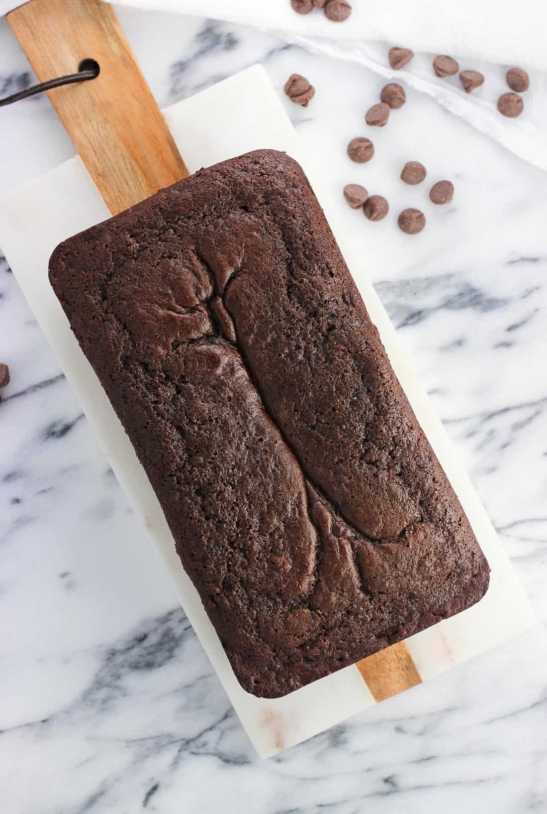 An overhead shot of a loaf of banana bread on a marble serving board before being sliced