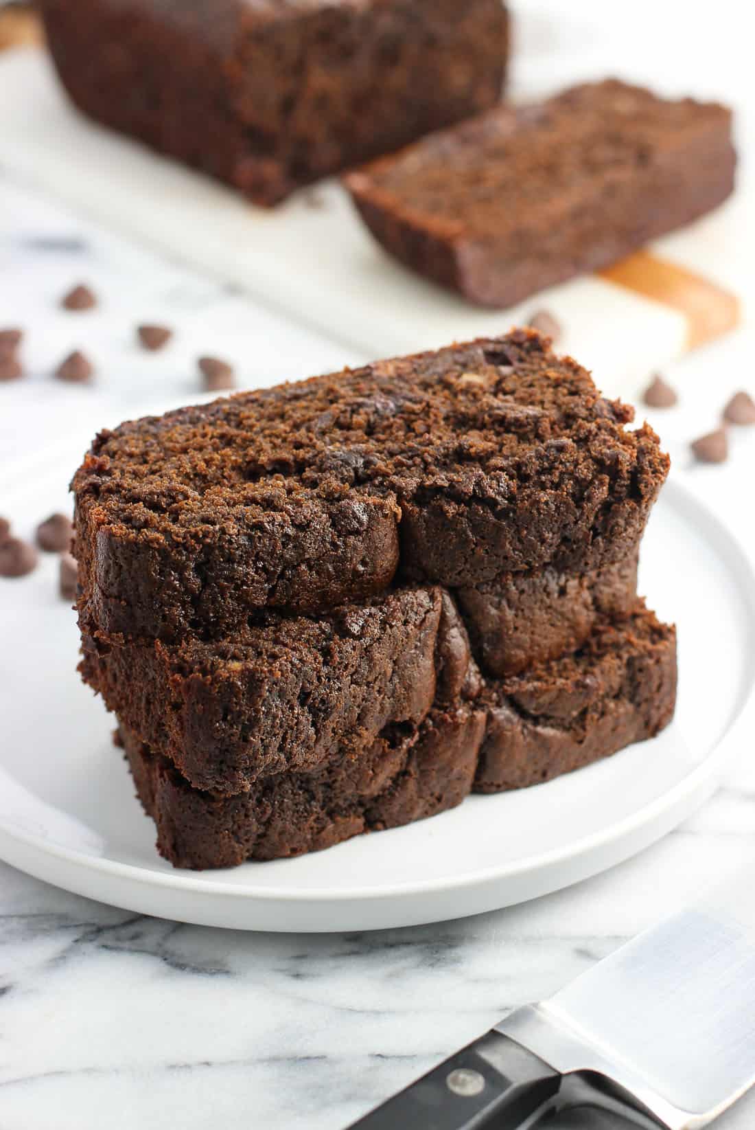 A stack of three slices of banana bread on a dessert bread with the rest of the loaf in the background