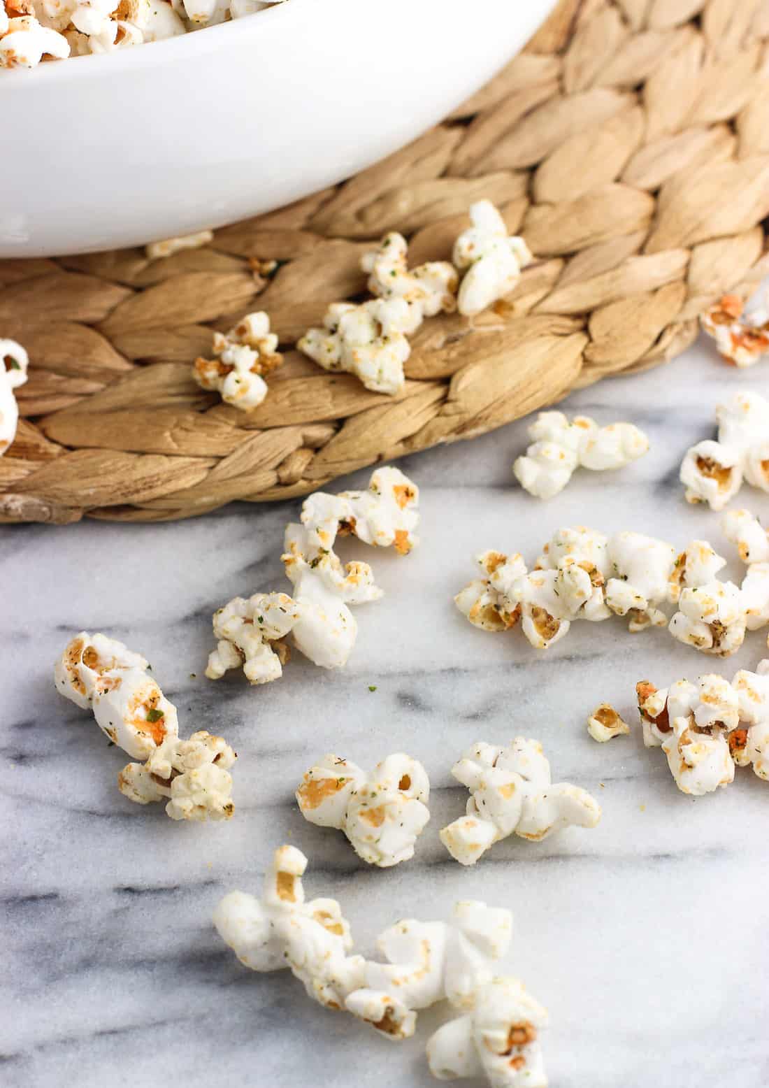 Seasoned popcorn loose on a marble board in front of the bowl.