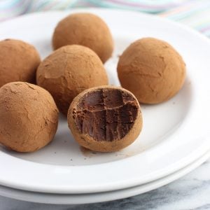 Six truffles coated in cocoa powder on a small dessert plate with a bite taken out of the front truffle