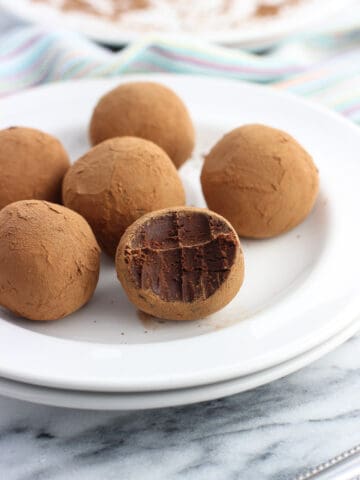 Six truffles coated in cocoa powder on a small dessert plate with a bite taken out of the front truffle