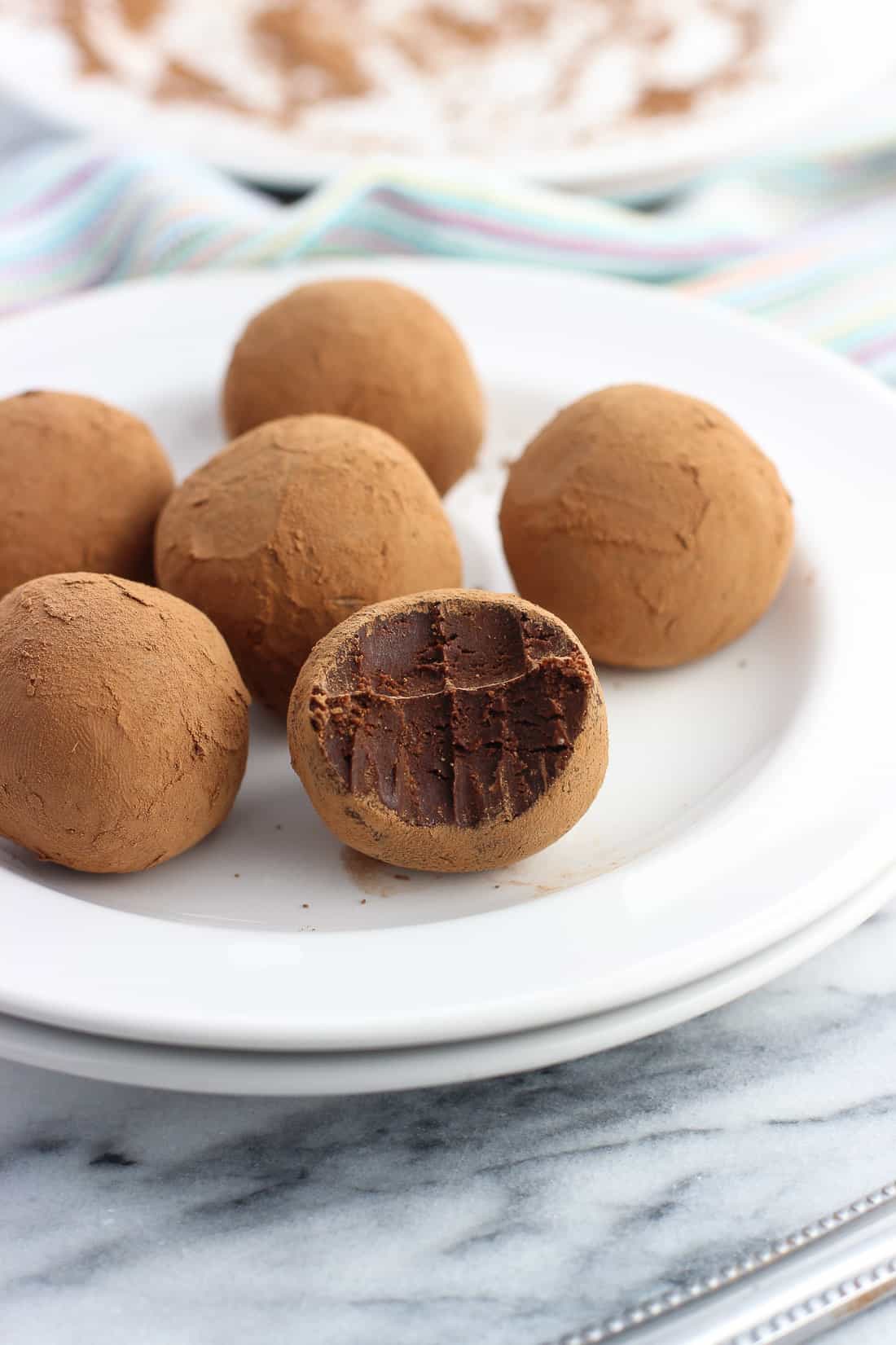 Six truffles coated in cocoa powder on a small dessert plate with a bite taken out of the front truffle