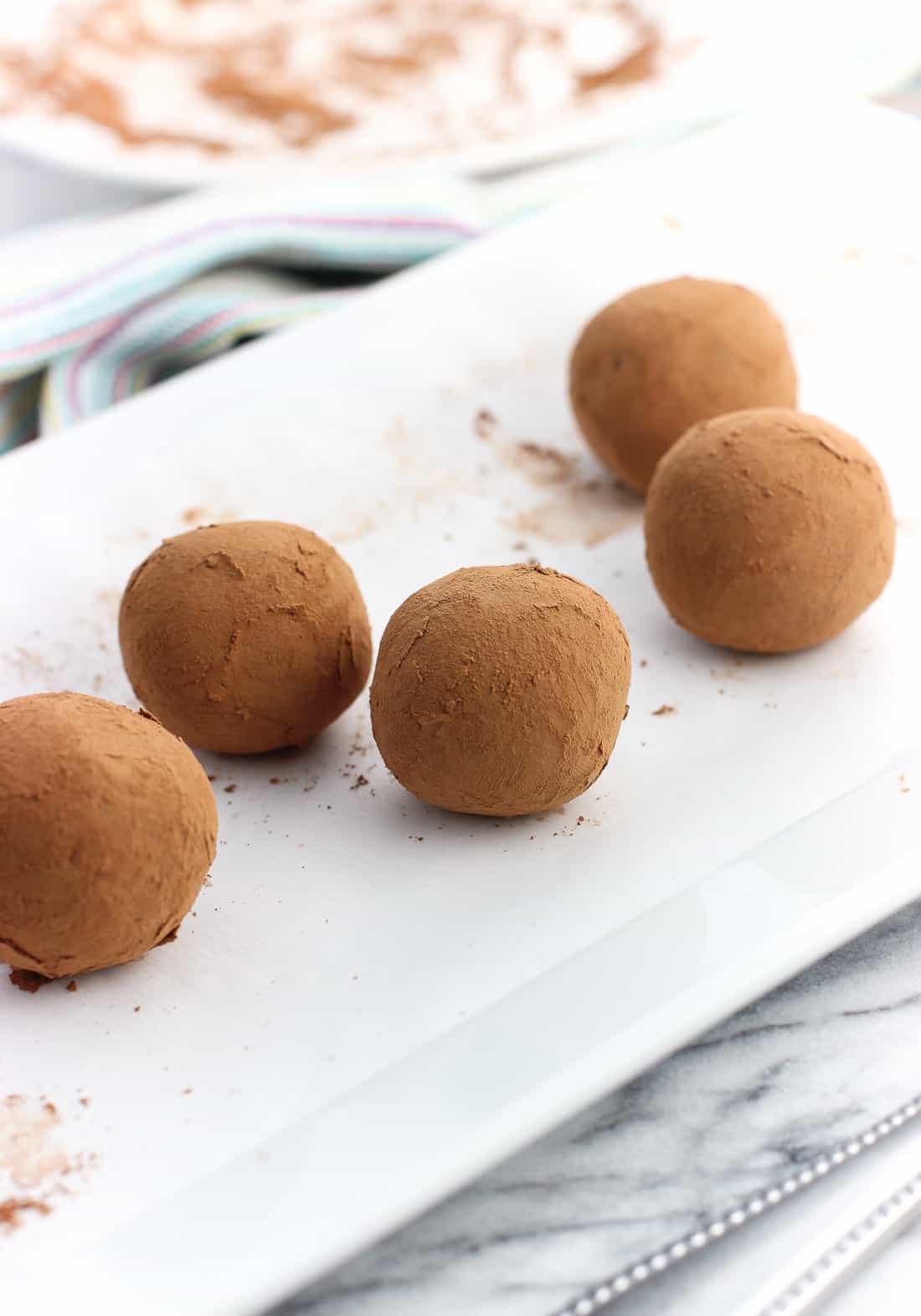 Five truffles rolled in cocoa powder on a rectangular ceramic serving tray