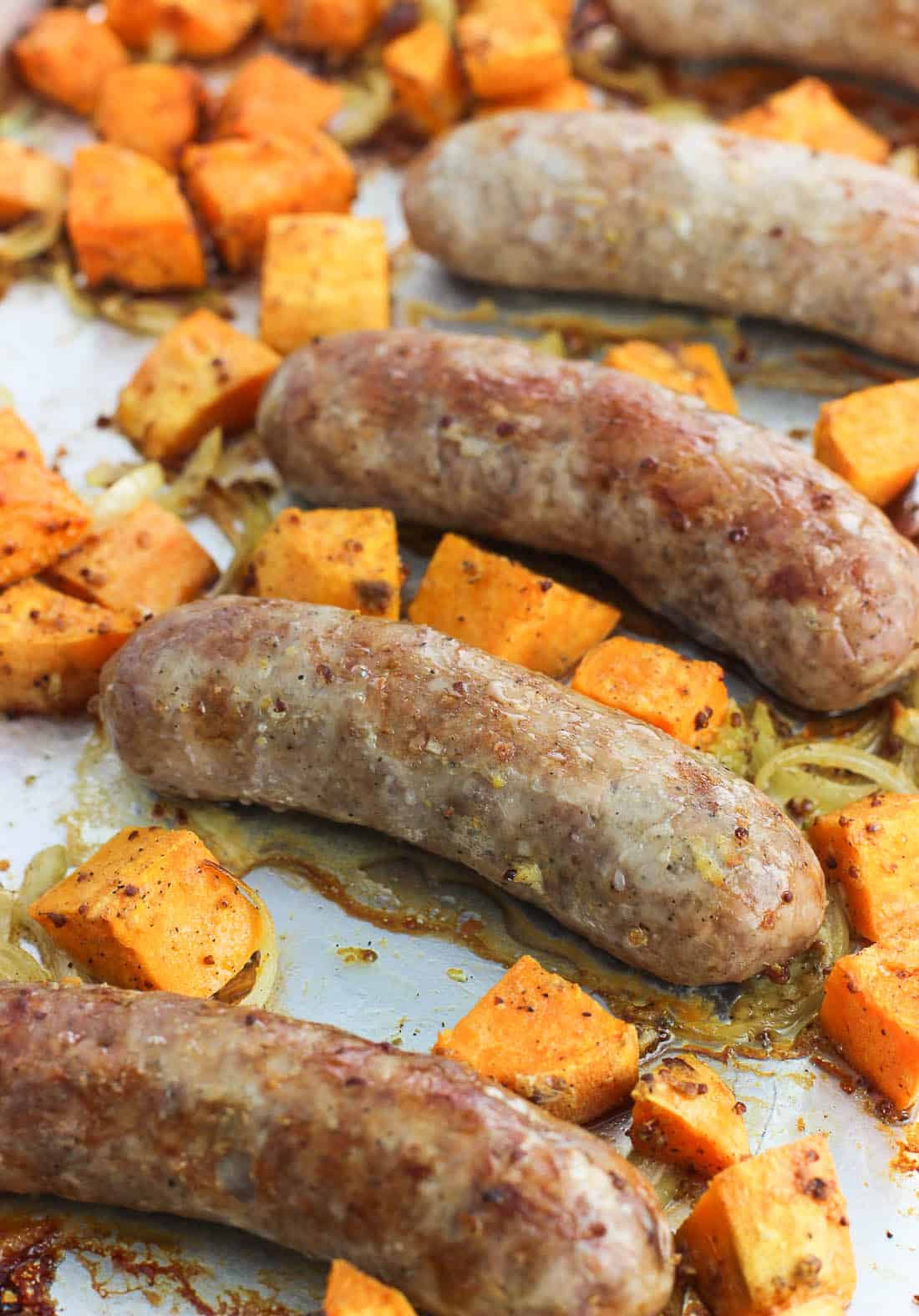Roasted bratwurst and sweet potatoes on a metal baking sheet after being cooked