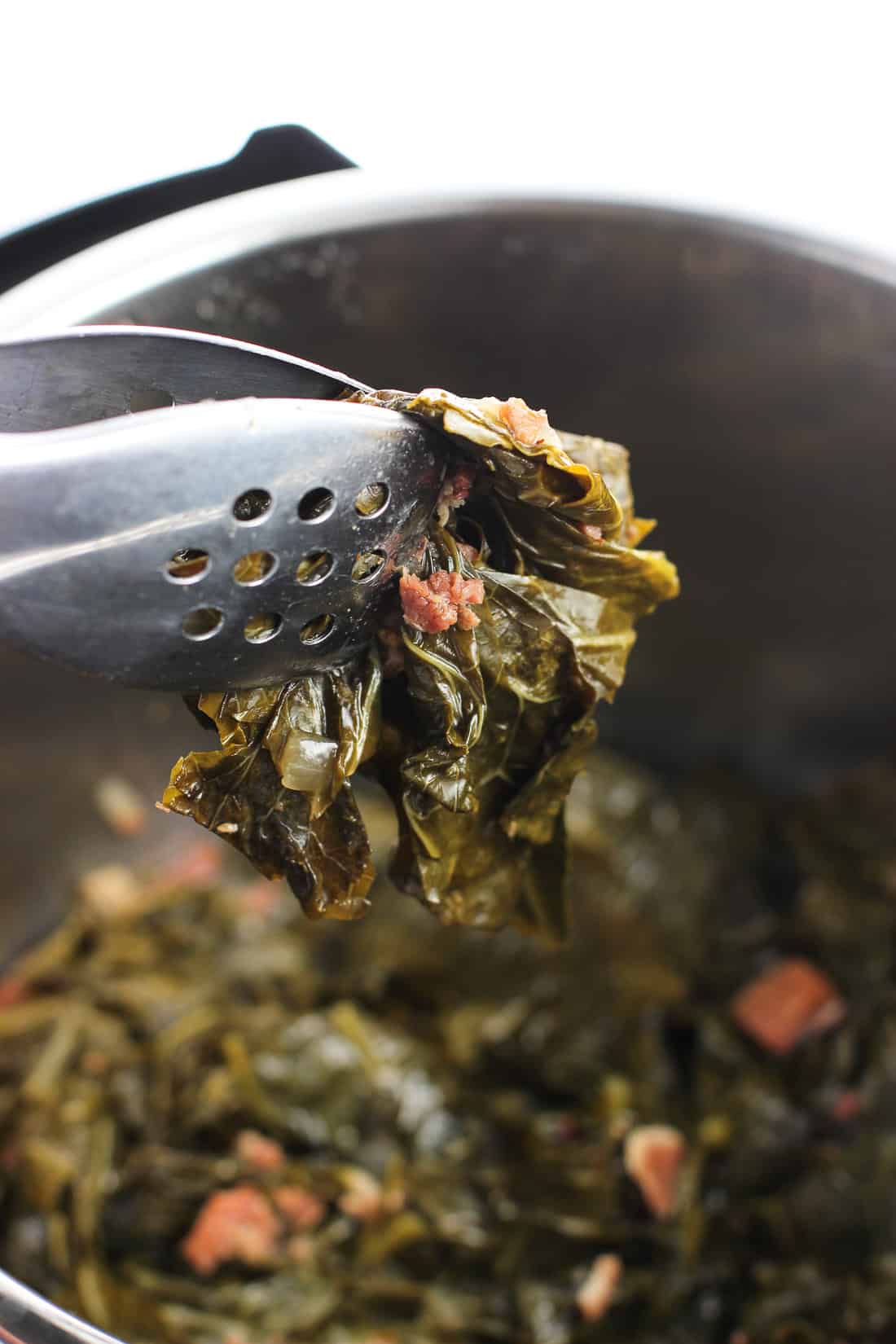 Tongs lifting collard greens out of the Instant Pot.