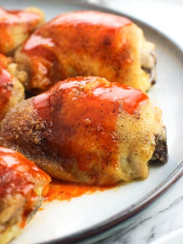 Buffalo sauce drizzled over baked chicken thighs on a plate.