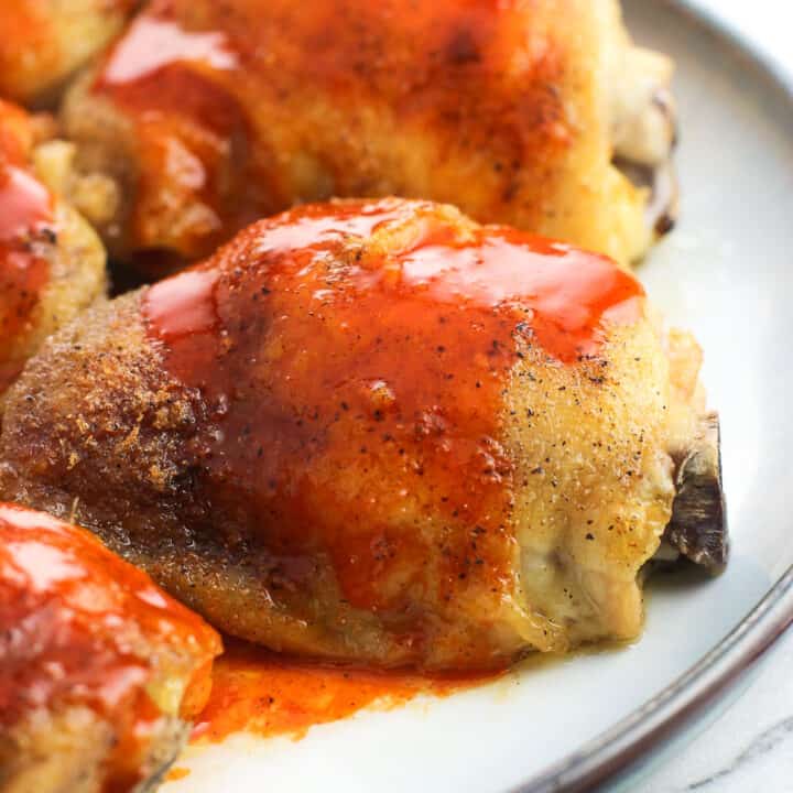 Buffalo sauce drizzled over baked chicken thighs on a plate.