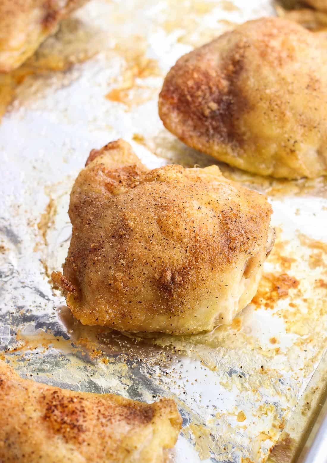 Baked chicken thighs on a foil-lined baking sheet.