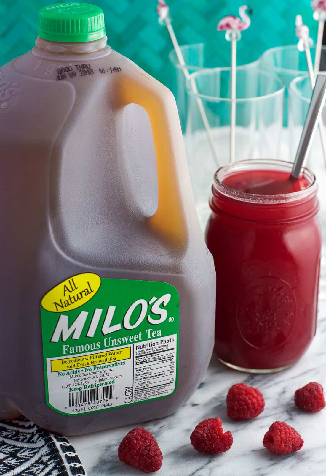 A gallon of Milo's Iced Tea next to a jar of honey raspberry syrup