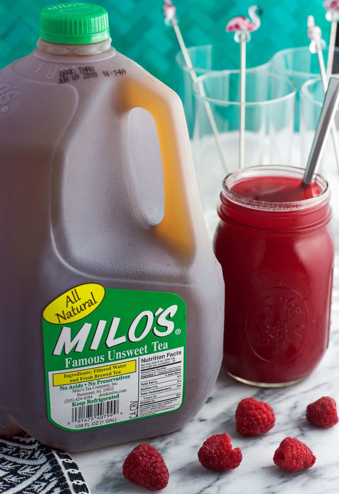 A gallon of Milo's Iced Tea next to a jar of honey raspberry syrup.