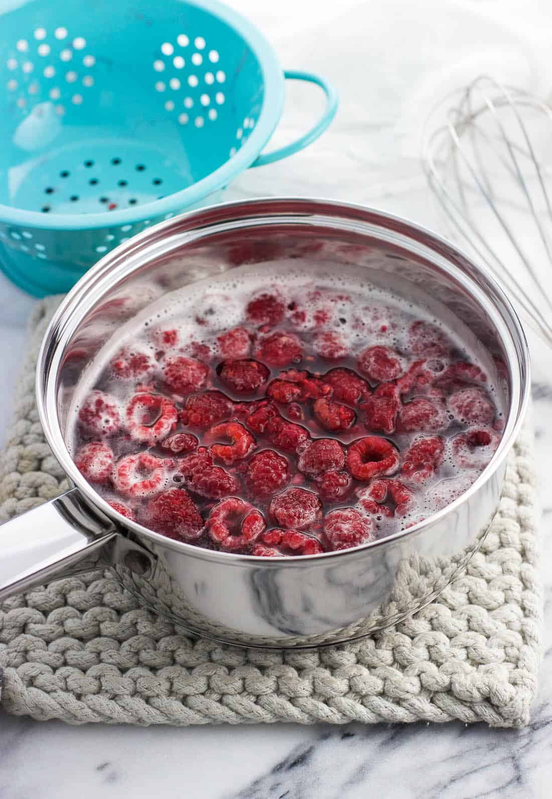 Whole raspberries in the syrup liquid in a medium metal saucepan.