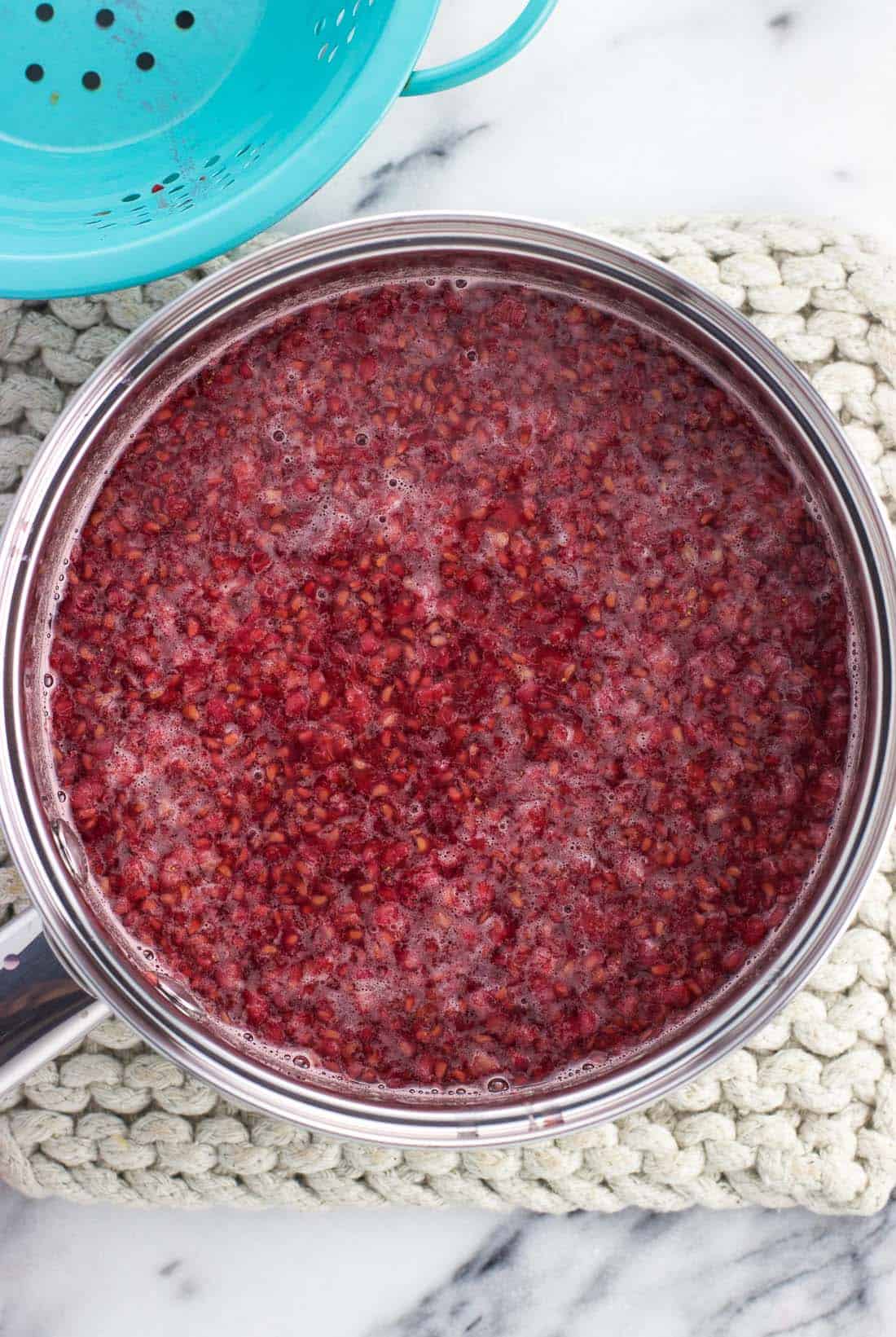 Smashed raspberries steeping in syrup in a medium saucepan.