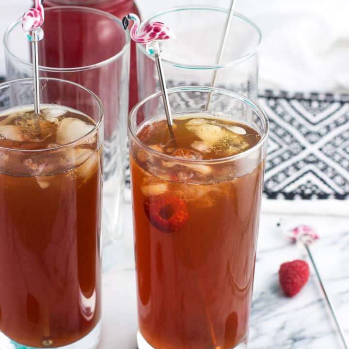 Glasses of iced tea garnished with fresh raspberries and flamingo drink stirrers.