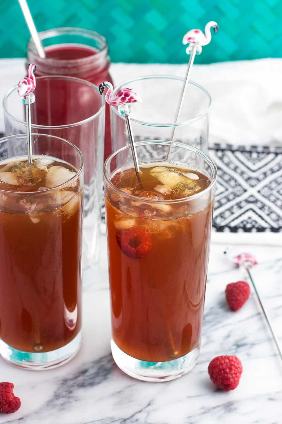 Glasses of iced tea garnished with fresh raspberries and flamingo drink stirrers.