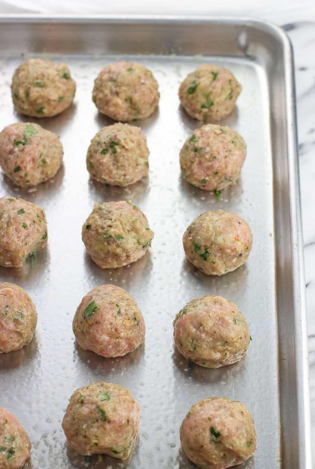 Raw turkey meatballs lined up on a greased baking sheet.