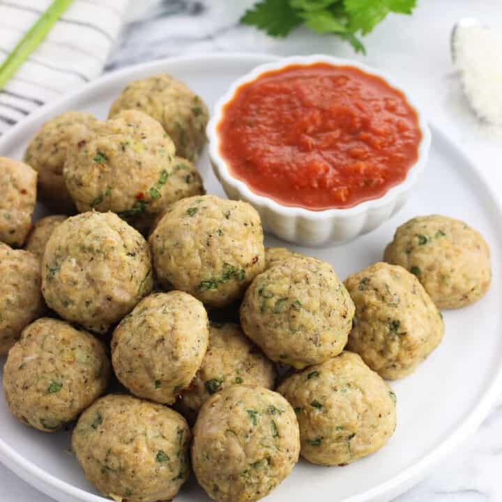 Turkey meatballs piled on a plate with a small bowl of marinara dipping sauce.