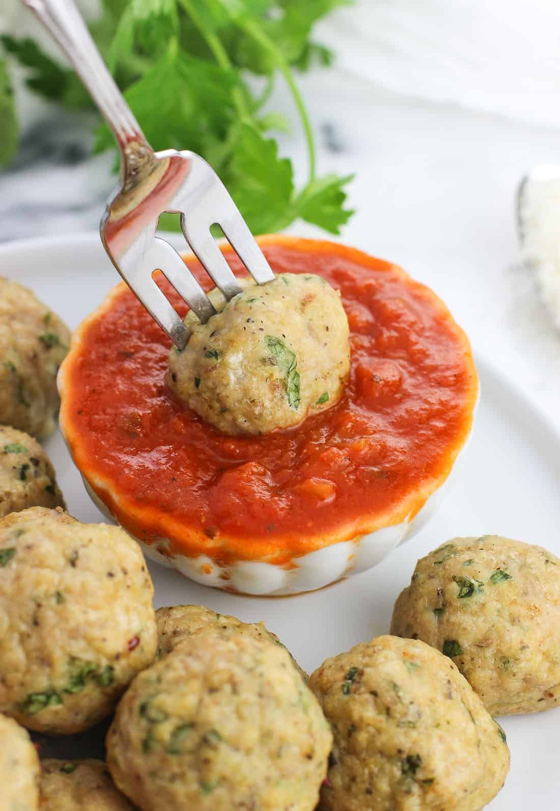 A fork dipping a meatball into the bowl of marinara sauce.
