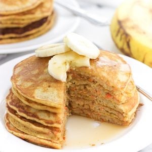 A stack of pancakes topped with banana slices on a plate with a wedge cut out.