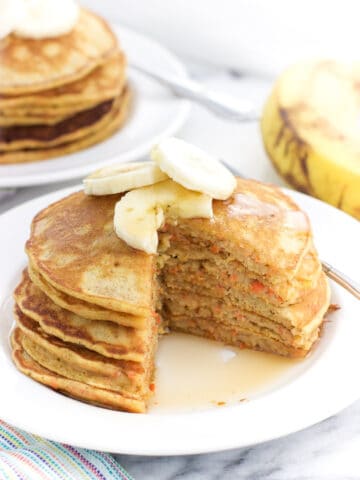 A stack of pancakes topped with banana slices on a plate with a wedge cut out.