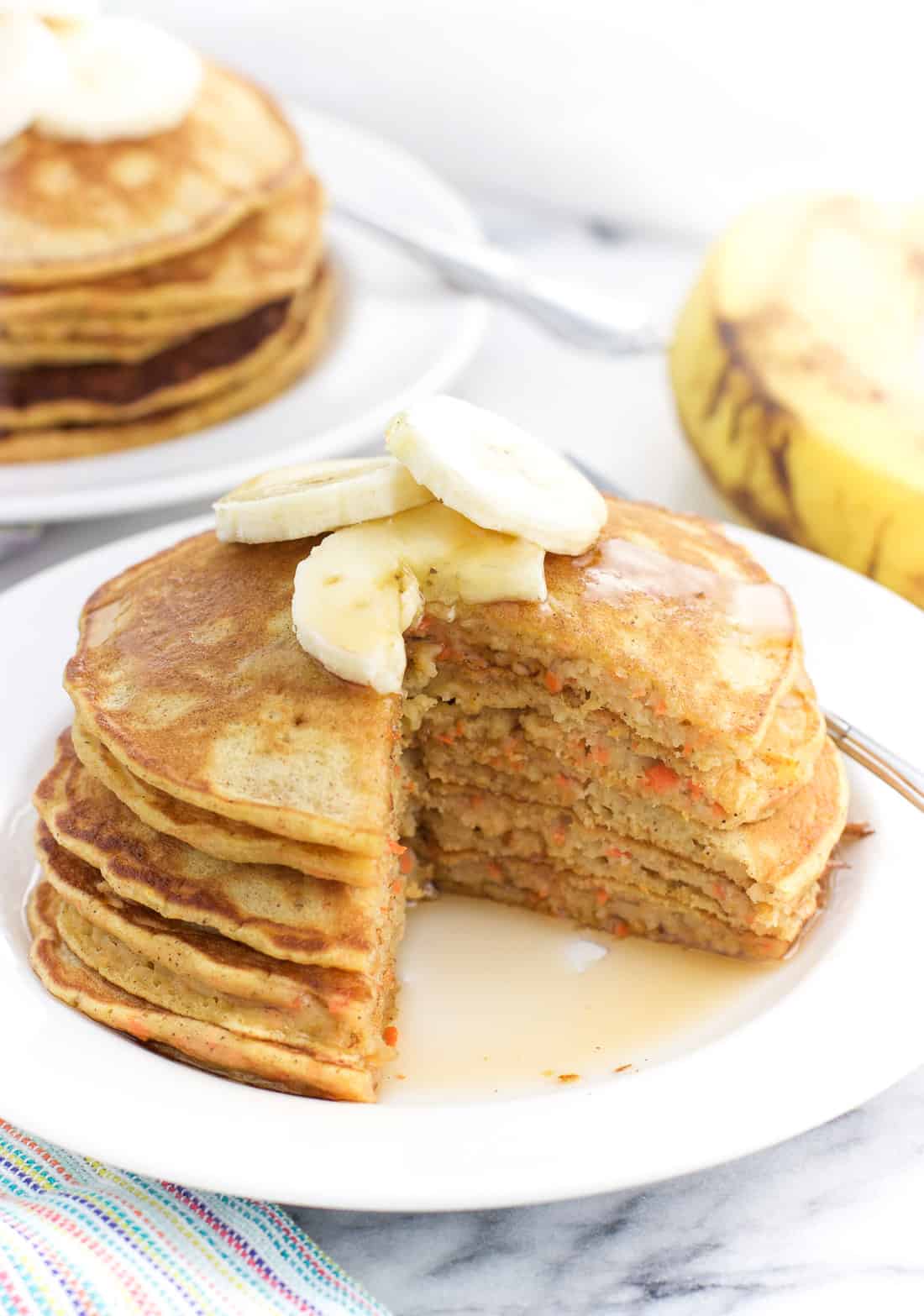 A stack of pancakes topped with banana slices on a plate with a wedge cut out.